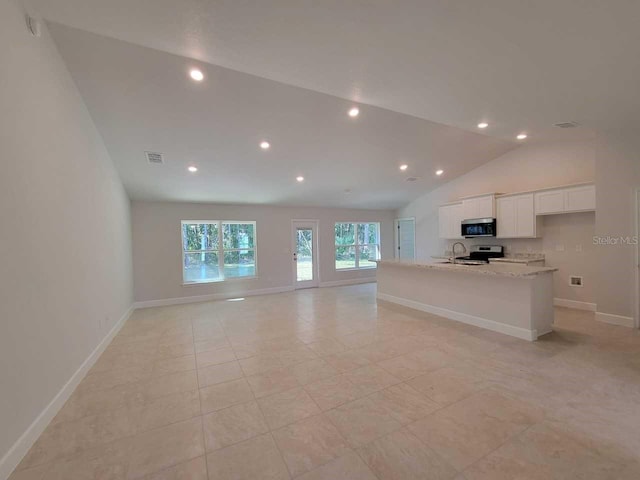 interior space featuring lofted ceiling, appliances with stainless steel finishes, an island with sink, white cabinets, and light stone counters