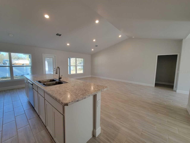 kitchen with vaulted ceiling, dishwasher, sink, a kitchen island with sink, and light stone counters