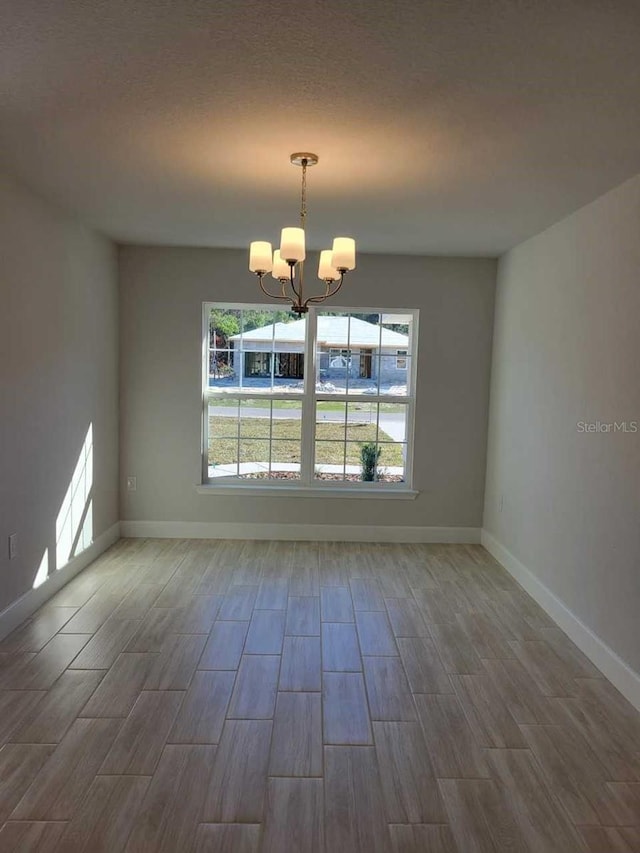 empty room with wood-type flooring, a notable chandelier, and a textured ceiling