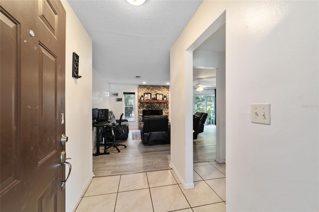 foyer with a stone fireplace, ceiling fan, light hardwood / wood-style floors, and a textured ceiling