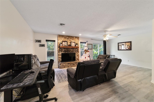 living room with a fireplace, a textured ceiling, light hardwood / wood-style flooring, and ceiling fan