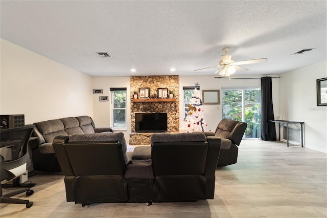 living room featuring a textured ceiling, a stone fireplace, and ceiling fan