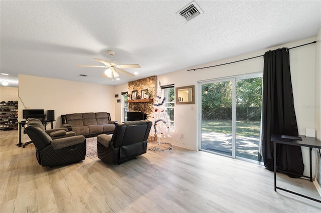 living room featuring a stone fireplace, ceiling fan, light hardwood / wood-style flooring, and a textured ceiling