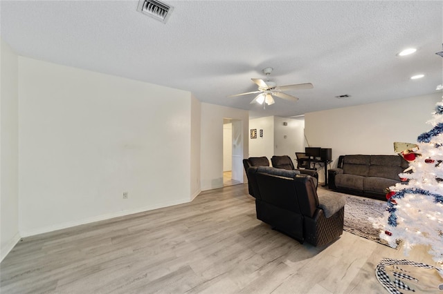 living room featuring ceiling fan, light hardwood / wood-style floors, and a textured ceiling