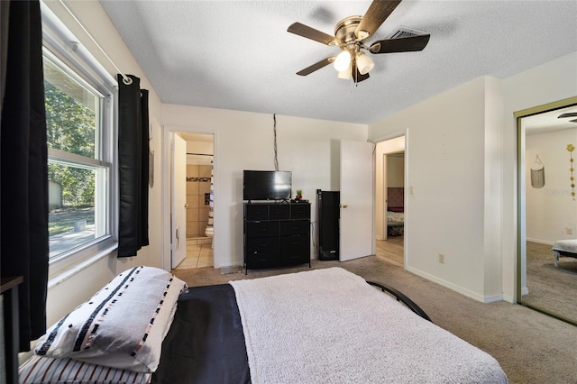 bedroom featuring light carpet, ceiling fan, a textured ceiling, connected bathroom, and a closet