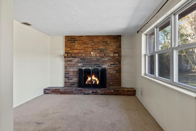 unfurnished living room with a textured ceiling, a fireplace, visible vents, and carpet flooring