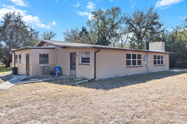 view of front of property featuring central AC, a chimney, a front lawn, and stucco siding