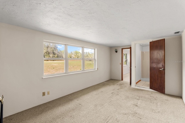 spare room with light carpet, a textured ceiling, and visible vents