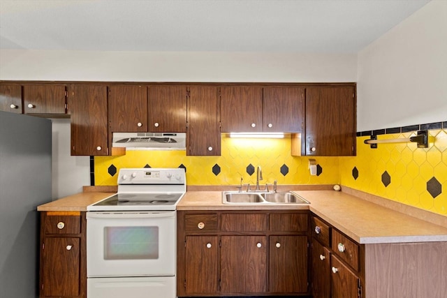 kitchen with electric stove, light countertops, freestanding refrigerator, a sink, and under cabinet range hood