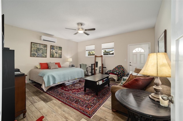 bedroom with a wall mounted AC, light hardwood / wood-style floors, and ceiling fan