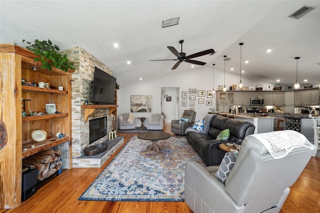 living room with a fireplace, light hardwood / wood-style flooring, ceiling fan, and lofted ceiling