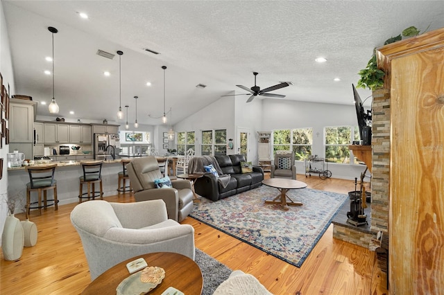 living room featuring ceiling fan, high vaulted ceiling, light hardwood / wood-style floors, and a textured ceiling