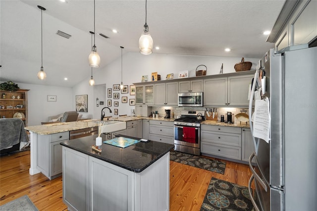 kitchen featuring appliances with stainless steel finishes, vaulted ceiling, light hardwood / wood-style flooring, a kitchen island, and hanging light fixtures