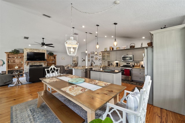 dining space with ceiling fan, light hardwood / wood-style flooring, a textured ceiling, vaulted ceiling, and a fireplace