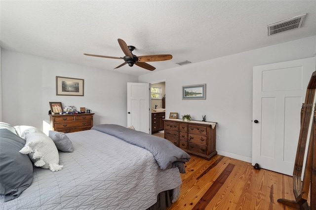 bedroom featuring a textured ceiling, ensuite bathroom, light hardwood / wood-style flooring, and ceiling fan