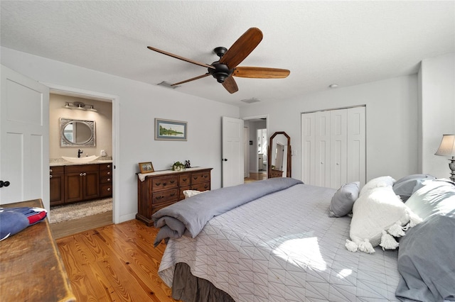 bedroom featuring ensuite bathroom, sink, light hardwood / wood-style flooring, ceiling fan, and a closet