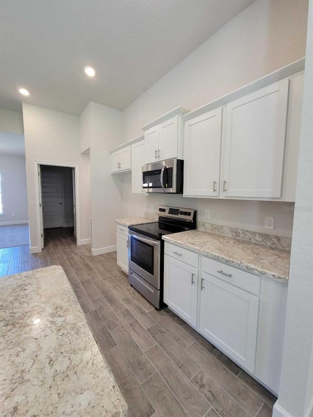 kitchen with appliances with stainless steel finishes, light hardwood / wood-style flooring, white cabinetry, and light stone counters