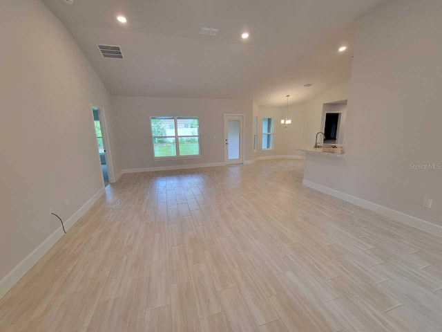 unfurnished living room featuring light wood-type flooring, visible vents, lofted ceiling, and baseboards