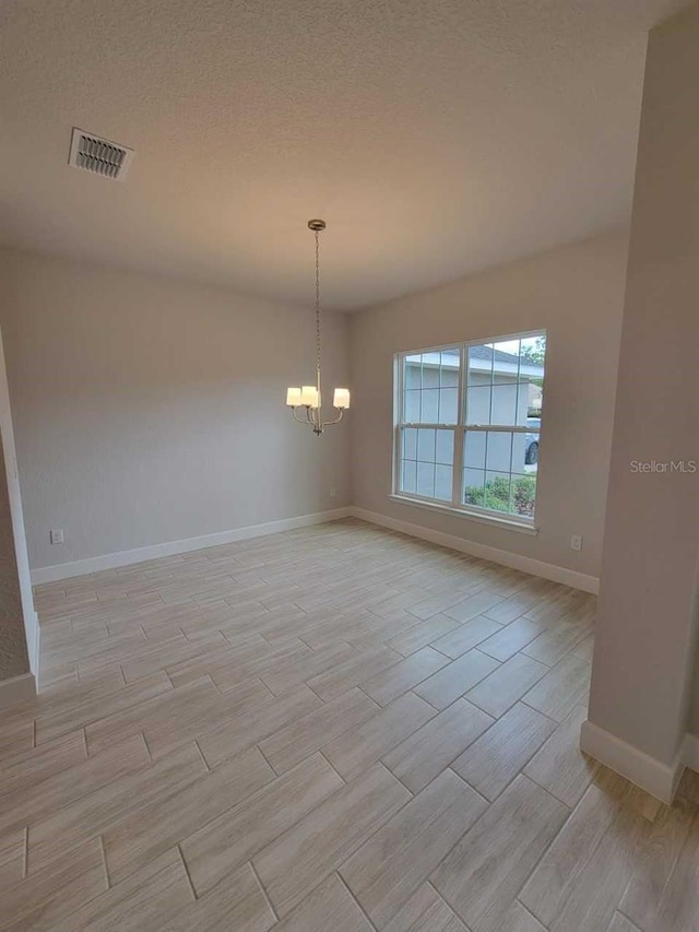 unfurnished room with a chandelier, baseboards, visible vents, wood finish floors, and a textured ceiling