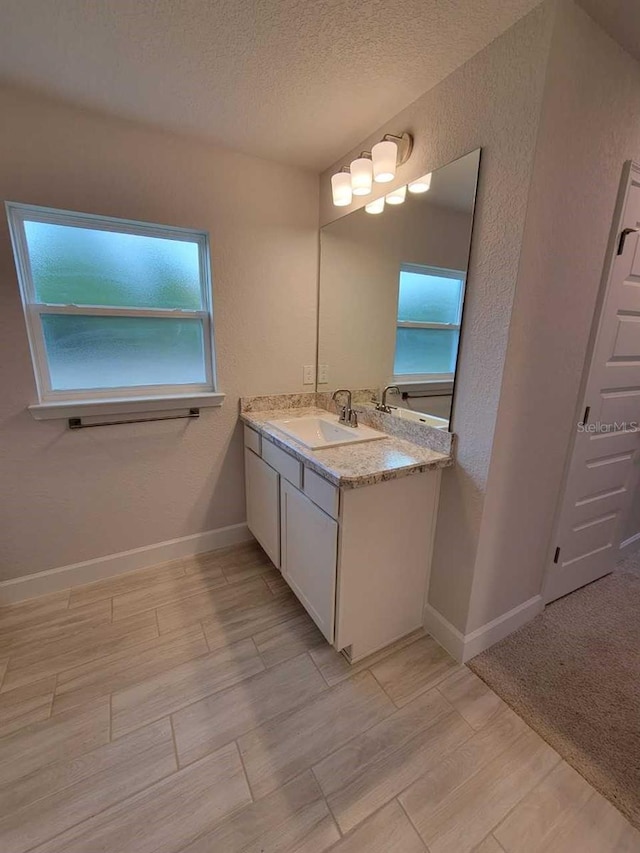 bathroom with a textured ceiling, a textured wall, vanity, and baseboards