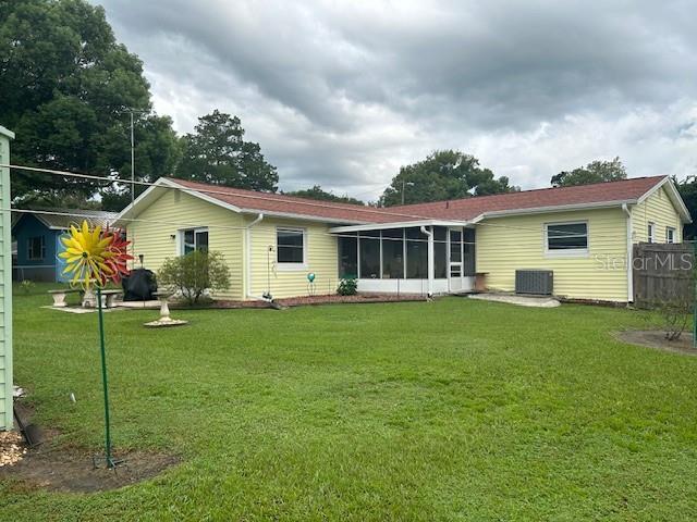 back of property featuring a lawn, central air condition unit, and a sunroom