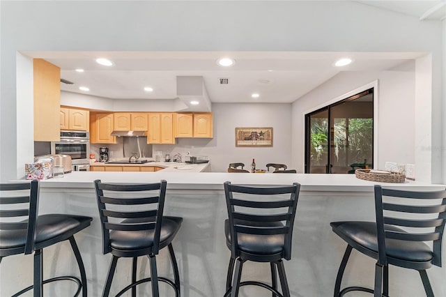 kitchen with a kitchen bar, kitchen peninsula, light brown cabinets, and black electric stovetop