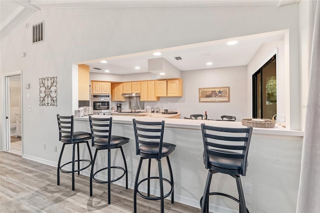 kitchen featuring a breakfast bar, light hardwood / wood-style floors, kitchen peninsula, and light brown cabinetry