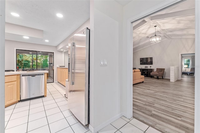 kitchen featuring light brown cabinets, stainless steel appliances, an inviting chandelier, lofted ceiling with beams, and light hardwood / wood-style floors