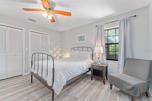 bedroom featuring multiple closets, ceiling fan, light hardwood / wood-style flooring, and a textured ceiling