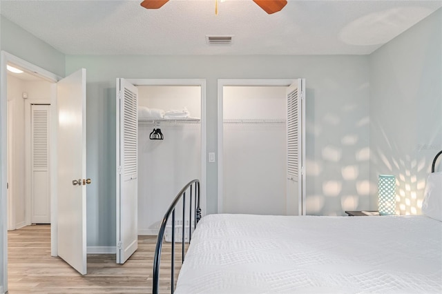 bedroom featuring multiple closets, ceiling fan, a textured ceiling, and light wood-type flooring