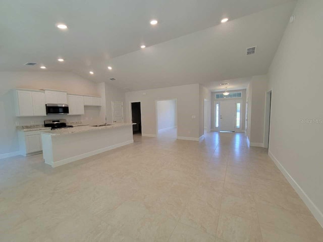 kitchen with light stone countertops, stainless steel appliances, lofted ceiling, a kitchen island with sink, and white cabinets