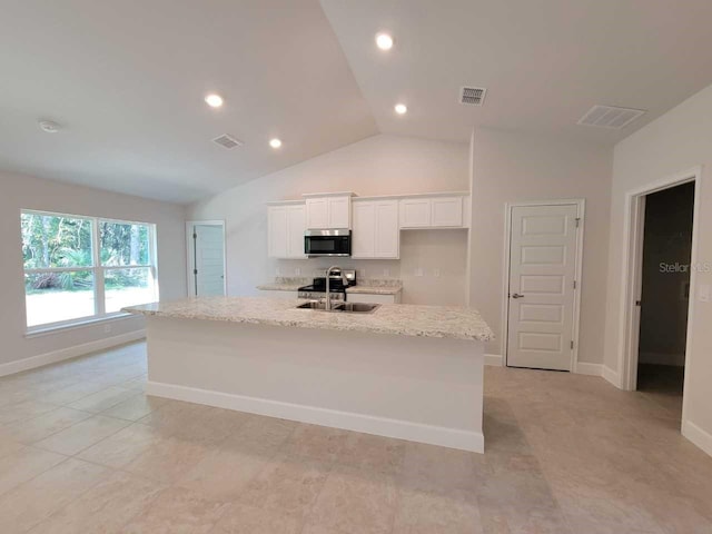 kitchen with lofted ceiling, white cabinets, sink, light stone countertops, and an island with sink