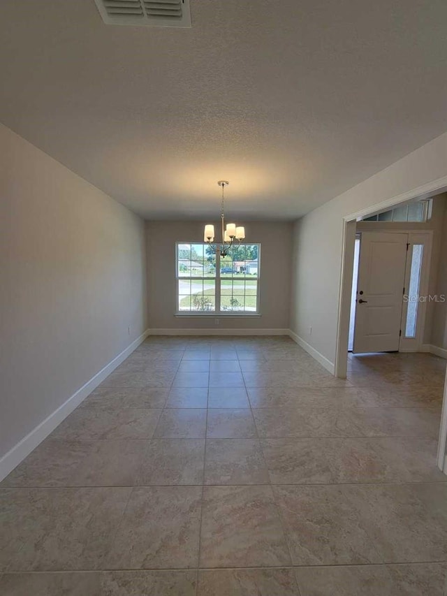 tiled empty room featuring a notable chandelier and a textured ceiling