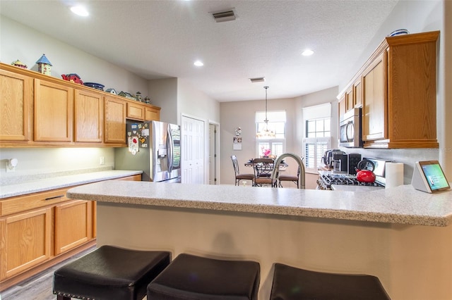 kitchen featuring kitchen peninsula, appliances with stainless steel finishes, a kitchen breakfast bar, decorative light fixtures, and a notable chandelier