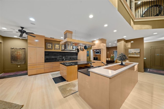 kitchen featuring a large island, ceiling fan, tasteful backsplash, light hardwood / wood-style floors, and exhaust hood