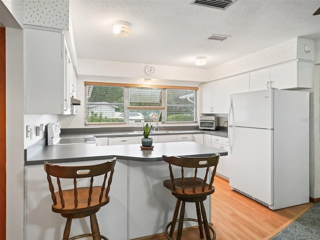 kitchen featuring white cabinets, stove, white fridge, and light hardwood / wood-style floors