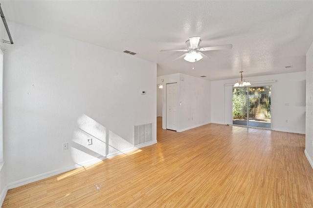 empty room with a textured ceiling, ceiling fan with notable chandelier, and light hardwood / wood-style flooring