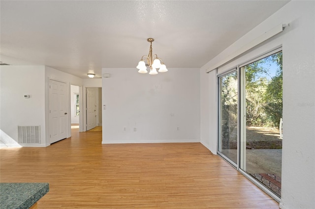 empty room with light hardwood / wood-style floors and an inviting chandelier