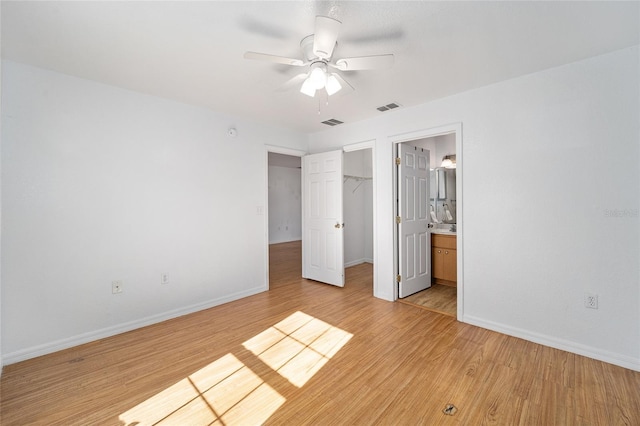 unfurnished bedroom featuring ensuite bathroom, a walk in closet, light hardwood / wood-style flooring, ceiling fan, and a closet