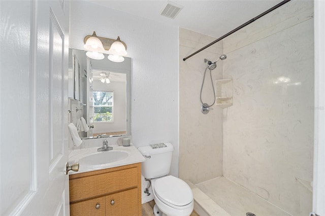 bathroom with a tile shower, vanity, toilet, and ceiling fan