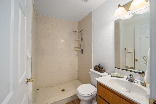 bathroom featuring a tile shower, vanity, a textured ceiling, and toilet