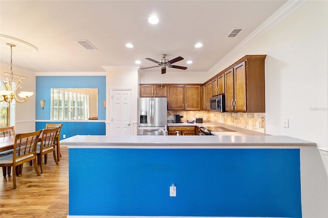 kitchen with ceiling fan with notable chandelier, hanging light fixtures, ornamental molding, appliances with stainless steel finishes, and kitchen peninsula