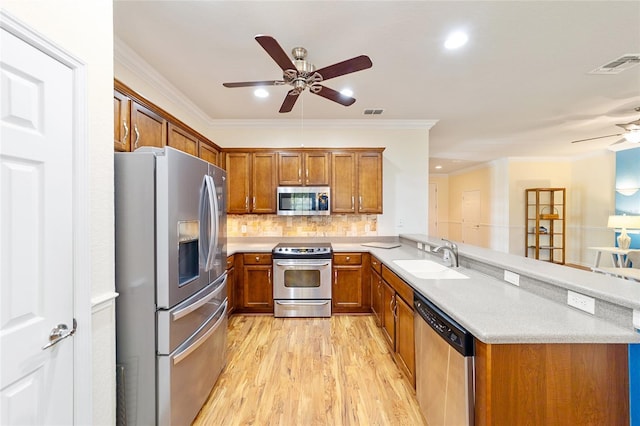 kitchen featuring kitchen peninsula, appliances with stainless steel finishes, light wood-type flooring, ornamental molding, and sink