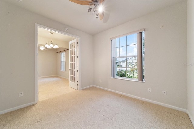 empty room featuring ceiling fan with notable chandelier, light carpet, and french doors