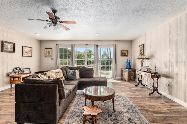 living room featuring ceiling fan, wood walls, light hardwood / wood-style floors, and a textured ceiling