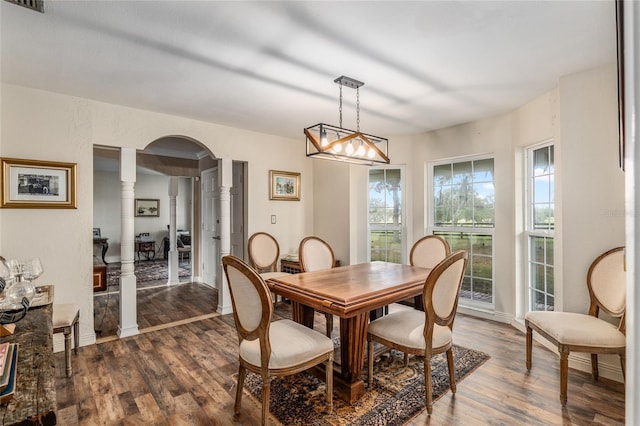 dining area with a healthy amount of sunlight, dark hardwood / wood-style flooring, ornate columns, and an inviting chandelier