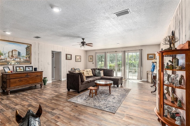 living room featuring hardwood / wood-style floors, a textured ceiling, ceiling fan, and wooden walls