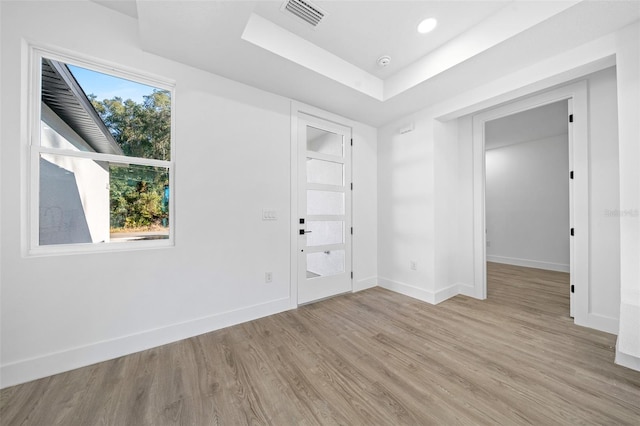 spare room with light hardwood / wood-style floors and a raised ceiling