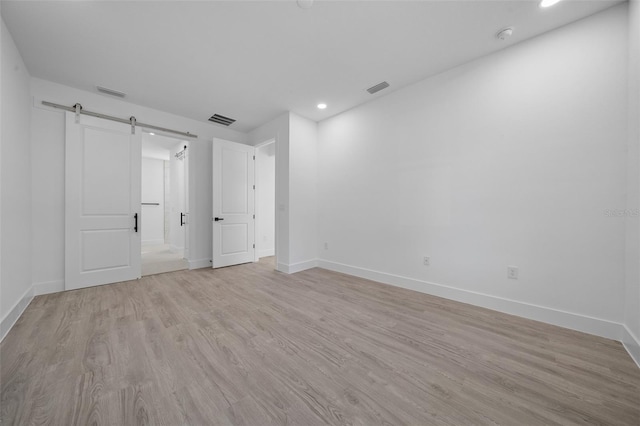 spare room with a barn door and light hardwood / wood-style flooring