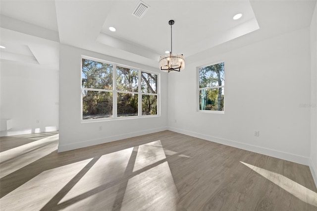 unfurnished dining area featuring hardwood / wood-style floors, a tray ceiling, and an inviting chandelier